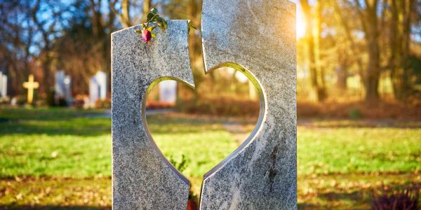 Broken heart-shaped tombstone with a rose in a cemetery at sunset.