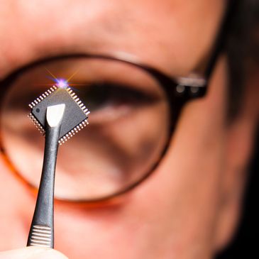 Person holding a microchip with tweezers in front of glasses.