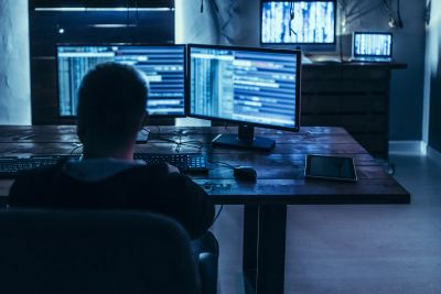 Person working on multiple monitors in a dimly lit room.
