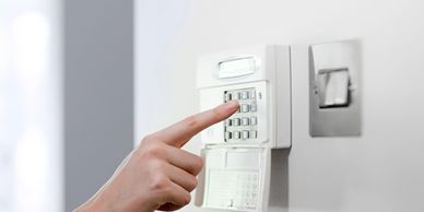 Hand pressing a button on a home security alarm keypad.