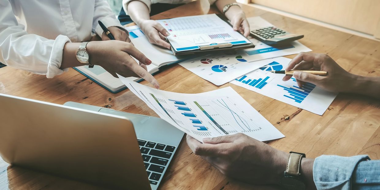 People analyzing financial charts and data around a laptop.