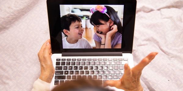 An elderly person video chatting joyfully with two children on a laptop.