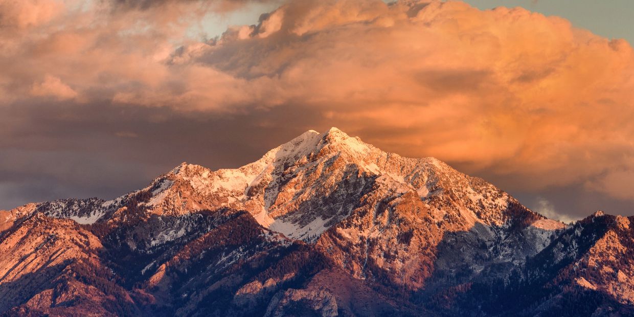 Snow-capped mountain at sunset with dramatic clouds.