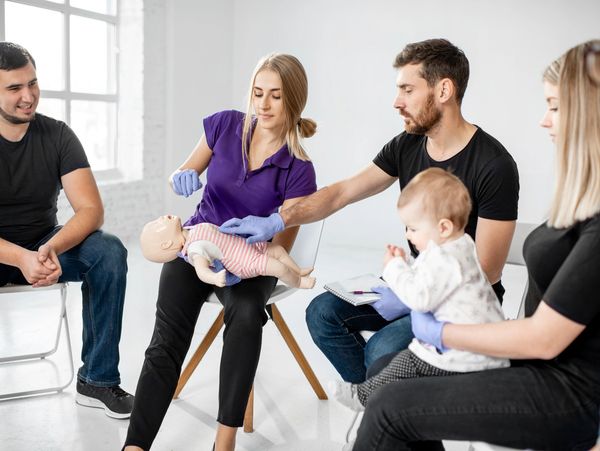 A group learning infant CPR using a baby mannequin in a bright room.