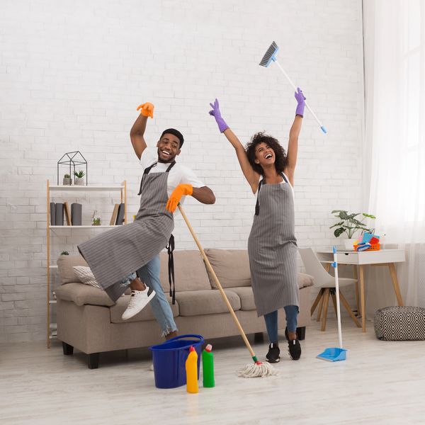 Happy couple dancing while cleaning their living room together.