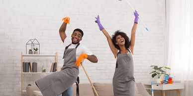 Happy couple in aprons dancing while cleaning their living room.