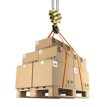 Pallet of cardboard boxes lifted by a yellow and black crane hook with orange straps.