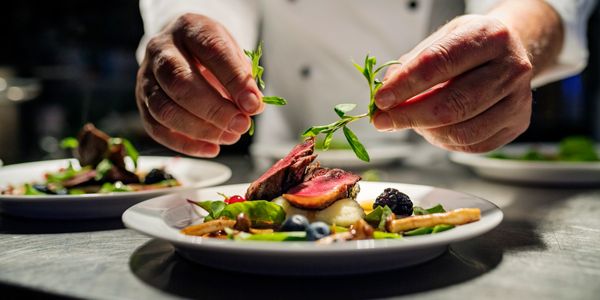 Chef garnishing a gourmet dish with fresh herbs in a professional kitchen.