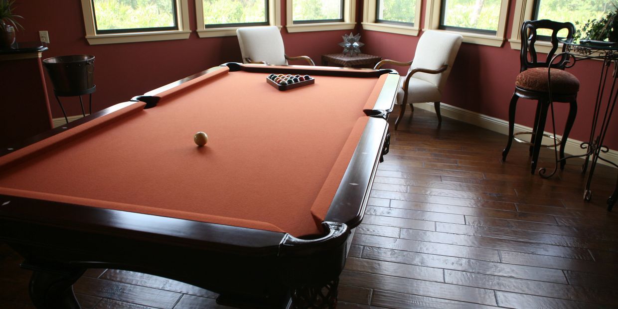 A stylish pool table with orange felt in a cozy room with large windows.