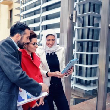 Three professionals reviewing documents and a tablet outdoors near a modern building.