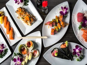 Variety of colorful sushi rolls and sashimi on elegant white plates with floral garnishes.