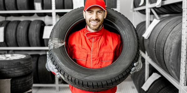 Smiling mechanic holding a tire in a tire storage room.
