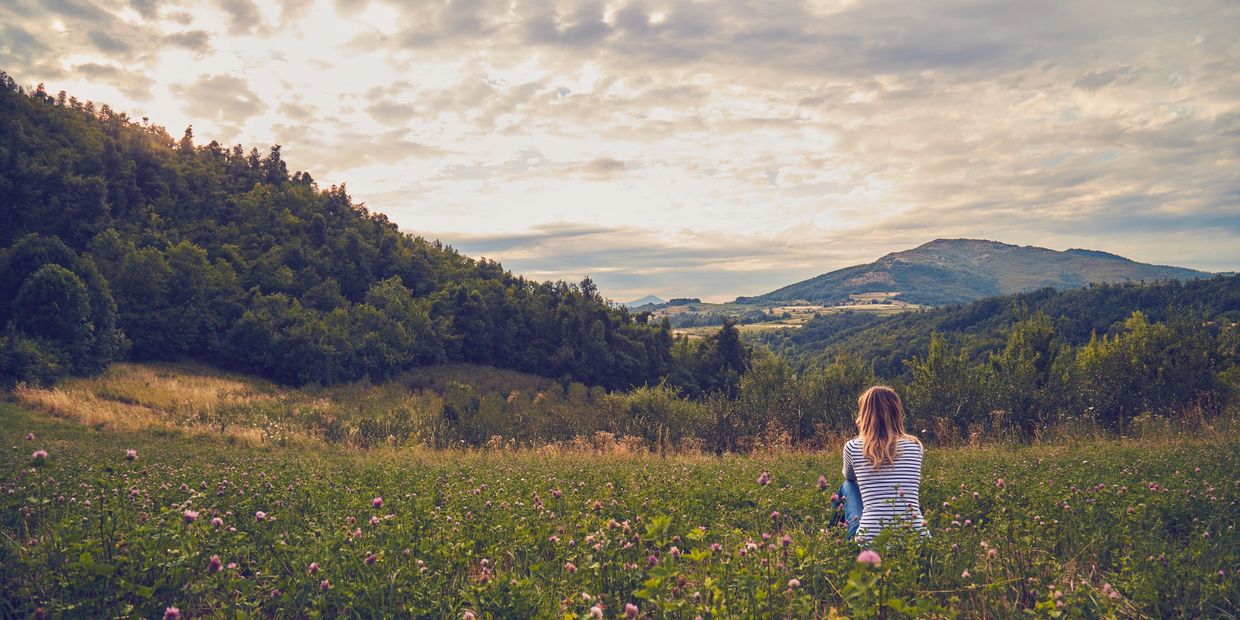 Woman sitting in a meadow, overlooking mountains.