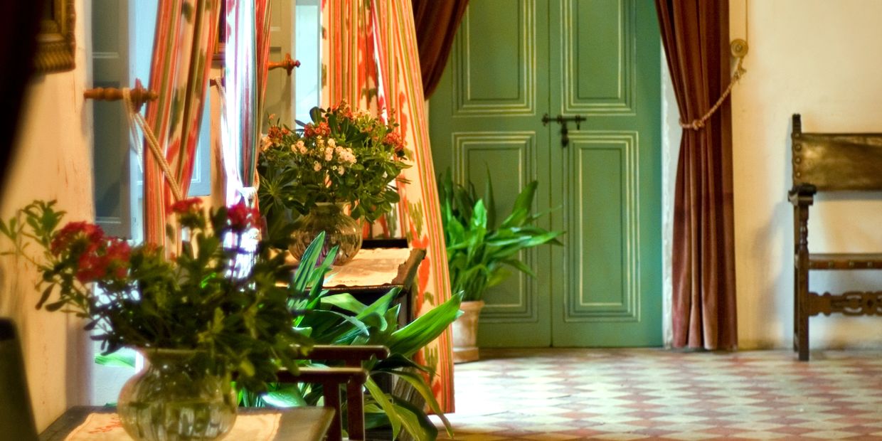 A bright hallway with plants, flowers, and green double doors at the end.
