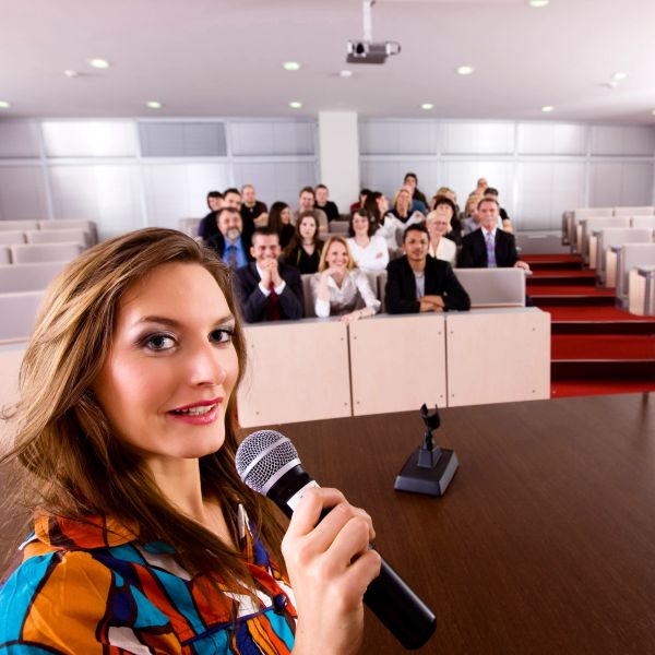 A woman speaking into a microphone to an audience in a lecture hall.