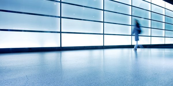 Blurred figure walking past a large illuminated glass wall in a modern space.