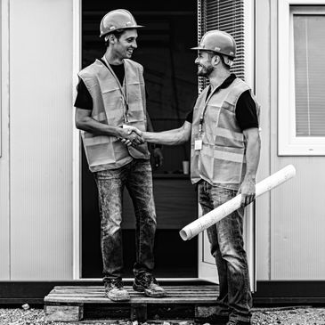 Two construction workers shaking hands outside a building site.
