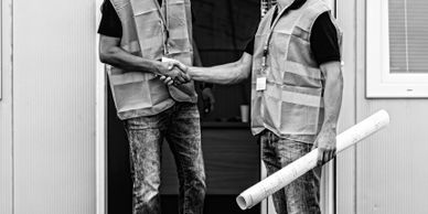 Two construction workers shaking hands outside a building site office.
