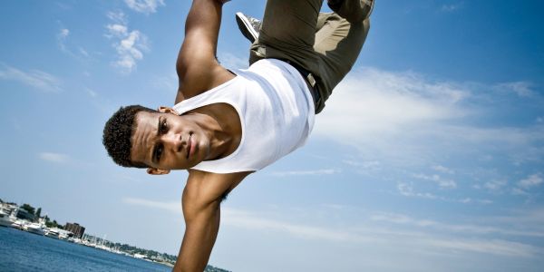 Young man doing an acrobatic move near water.