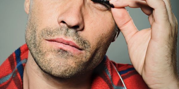 Man using an eyelash curler on his eyelashes.
