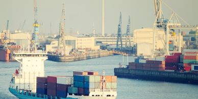 Cargo ship loaded with containers docked at a busy industrial port.