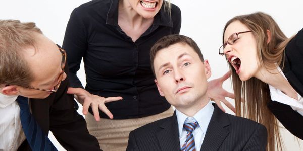 A man in a suit being yelled at by three angry coworkers.