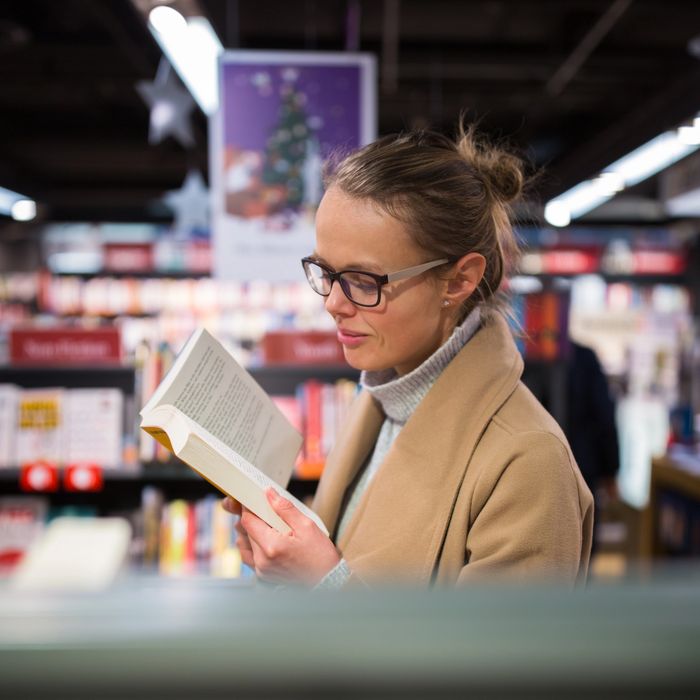 A woman reading a book in a bookstore.
