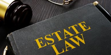 Close-up of an Estate Law book with a gavel and glasses on a dark table.
