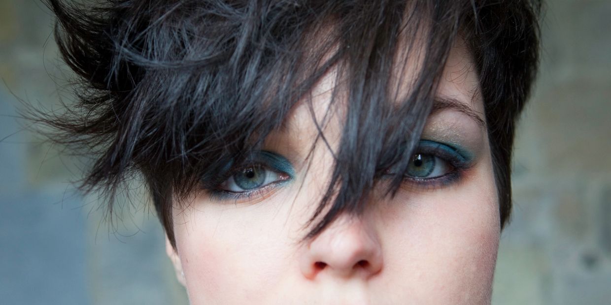 Model with a messy, textured dark pixie cut and striking teal eyeshadow.