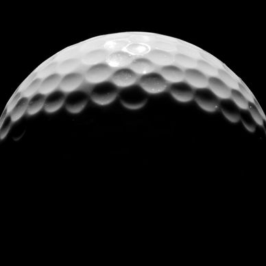 Close-up of a golf ball illuminated against a black background.