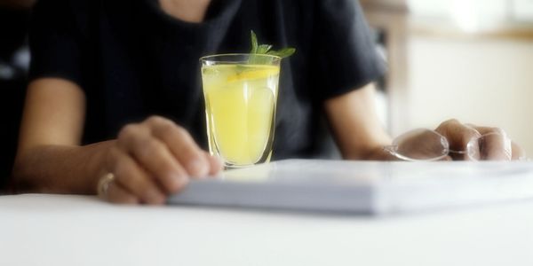 Person holding a glass of yellow drink with mint and lemon.