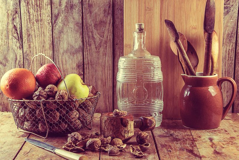 vintage kitchen utensils, jug, bottle, basket with fruits, nuts on the old wooden background in retro style