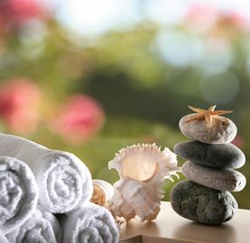Rolled white towels, seashells, and stacked stones with a starfish in a serene setting.