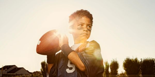 Young boy in football gear preparing to throw a football with sun flare.