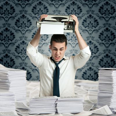 Frustrated man about to smash typewriter amidst piles of paper.