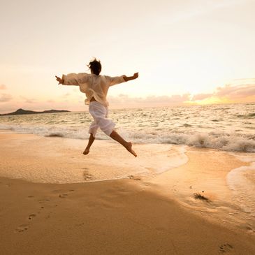 Person joyfully jumping on a beach during sunset.