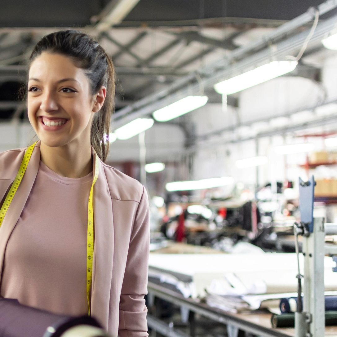 Smiling female fashion designer with measuring tape in a textile factory.