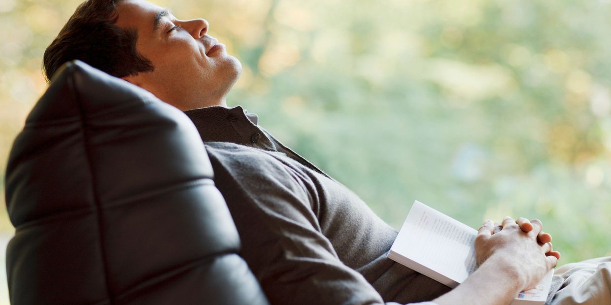 Man resting on a chair with a book in hand, eyes closed peacefully.