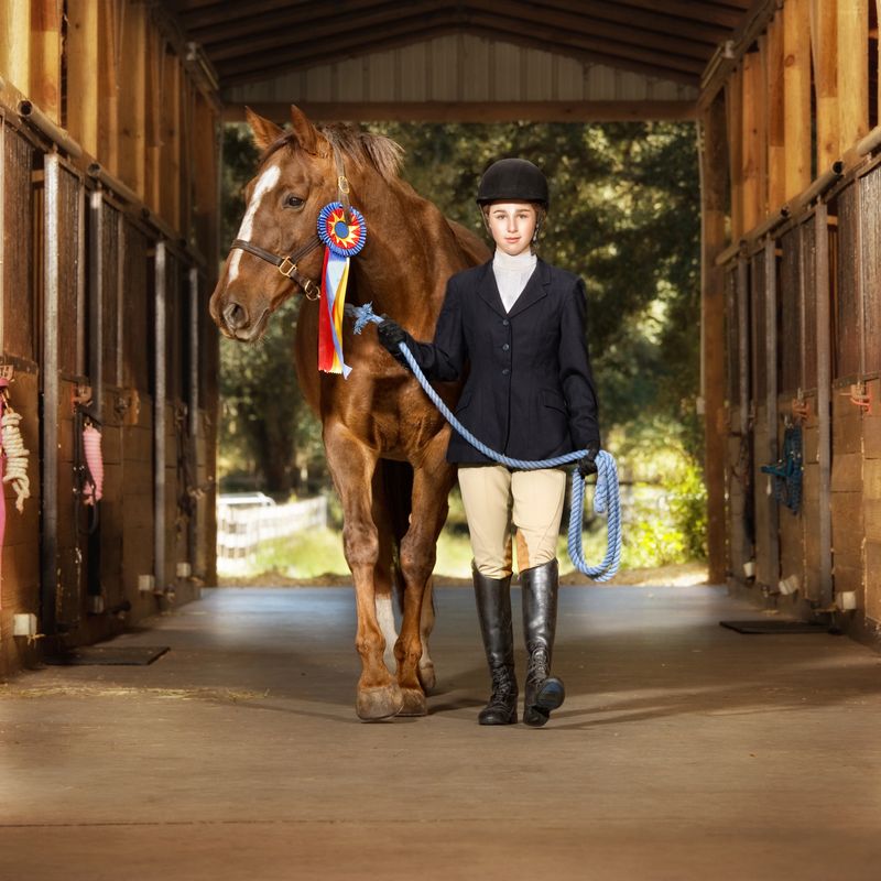 Young teenage female equestrian walking with her horse in the barn after winning an equestrian competition.
