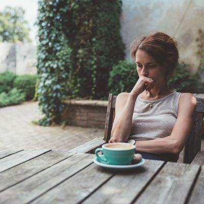 Woman sitting alone, lost in thought by a coffee cup.