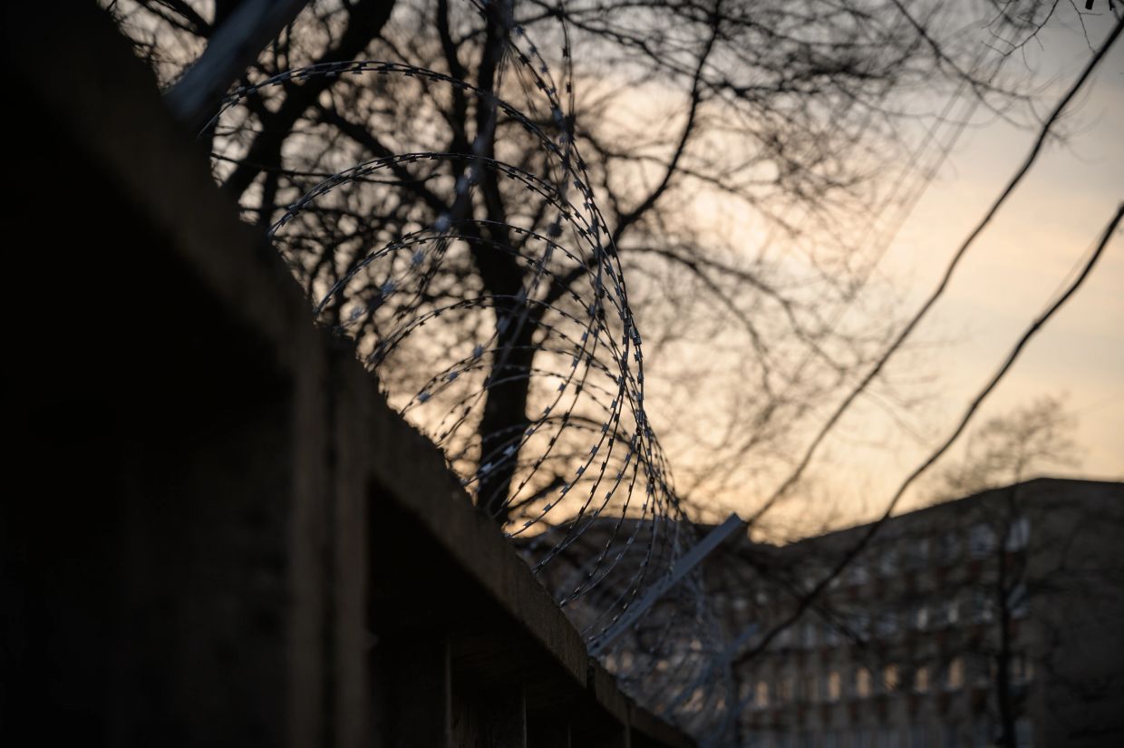 Barbed wire fence with trees and buildings in the background at sunset.