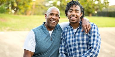 Two men smiling outdoors with arm around.