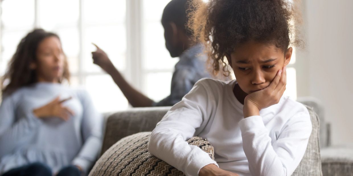 Sad child feeling upset during parents arguing in the background.