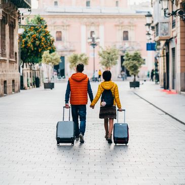 Couple walking hand in hand with suitcases on a city street.
