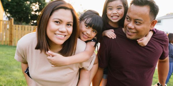 Happy family enjoying piggyback rides outdoors in a backyard.