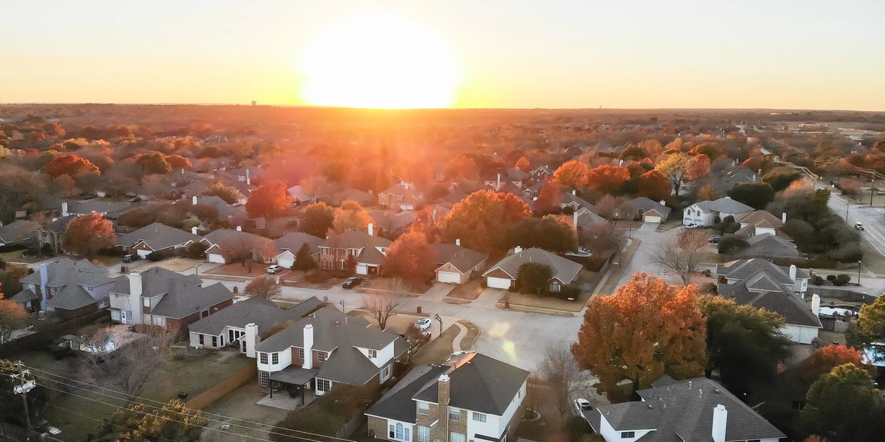 A suburban neighborhood at sunset with autumn trees and a backyard pool.
