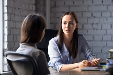 Two women having a serious conversation in an office setting.