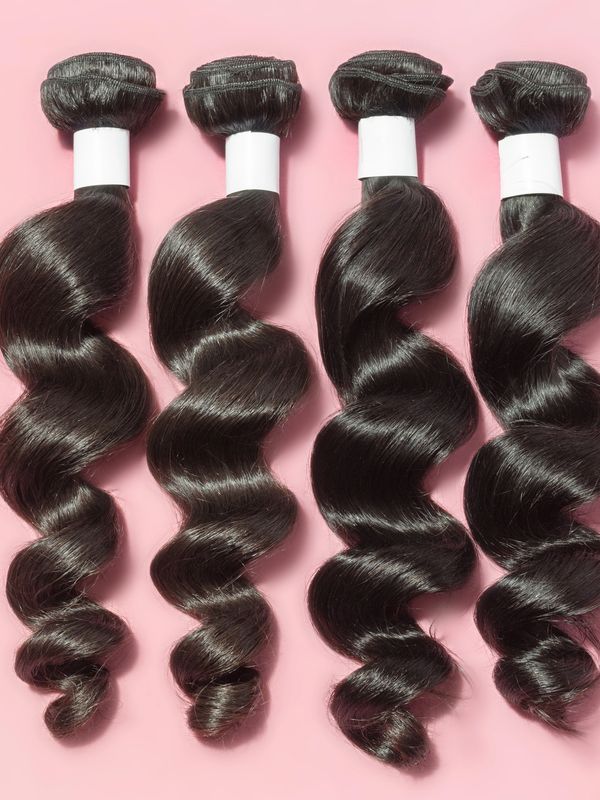 Four bundles of shiny curly black hair extensions on pink background