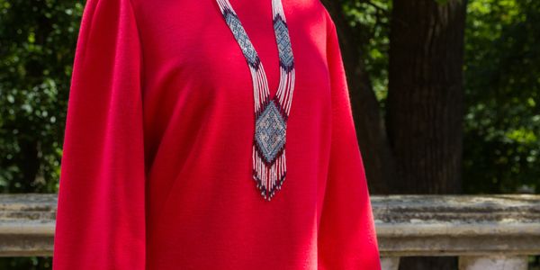Red dress on a mannequin with a beaded necklace outdoors.