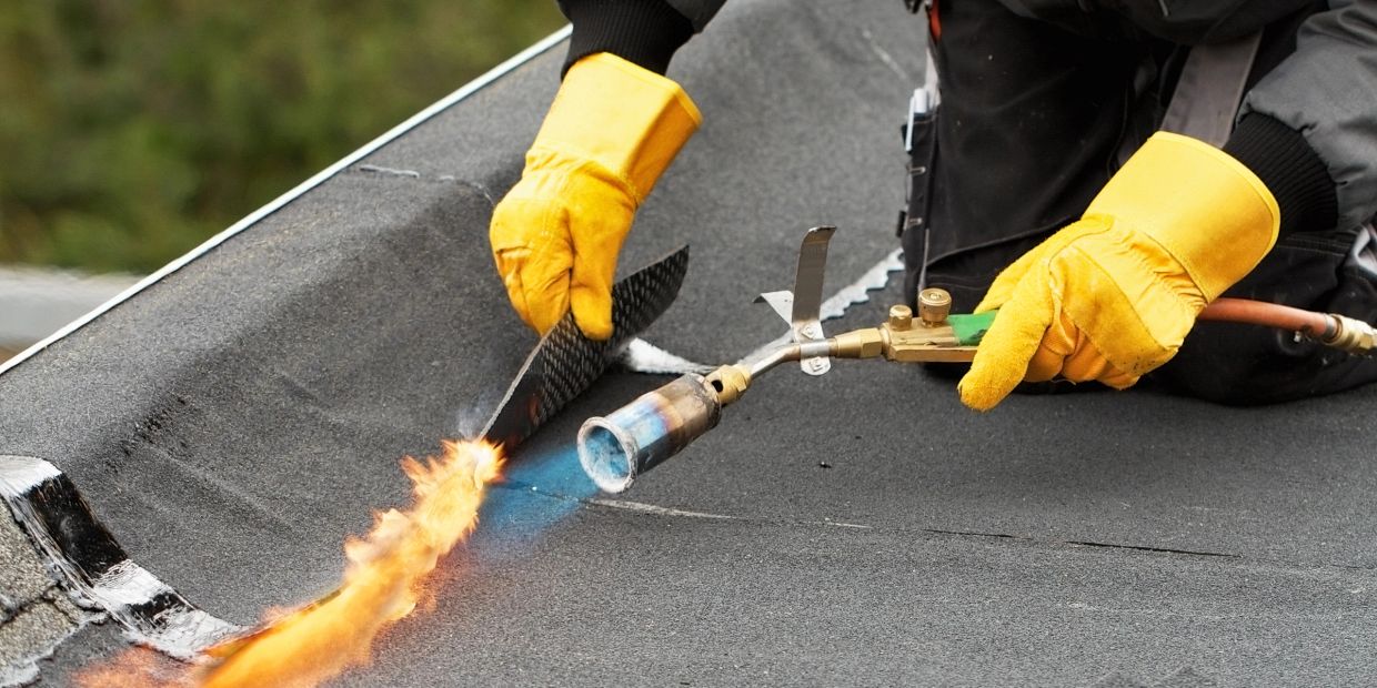 Worker uses a blowtorch to apply roofing material on a flat roof.
